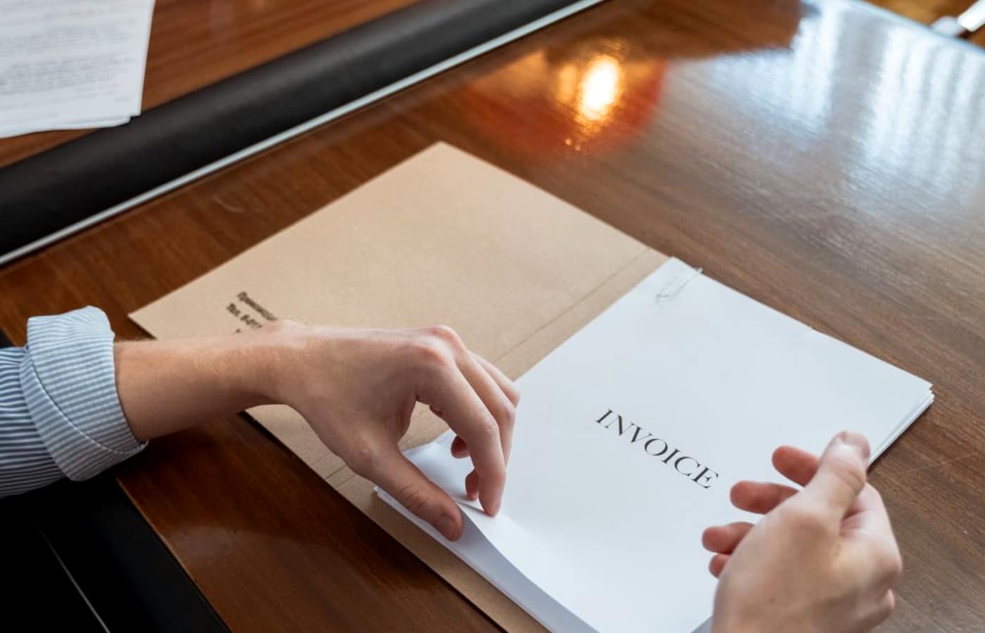 A person's hands holding a document clearly marked INVOICE at a desk