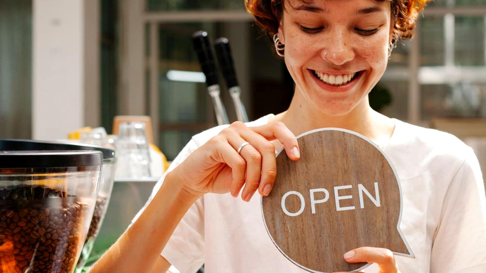 A small business owner smiling while holding an OPEN sign in the doorway of a shop