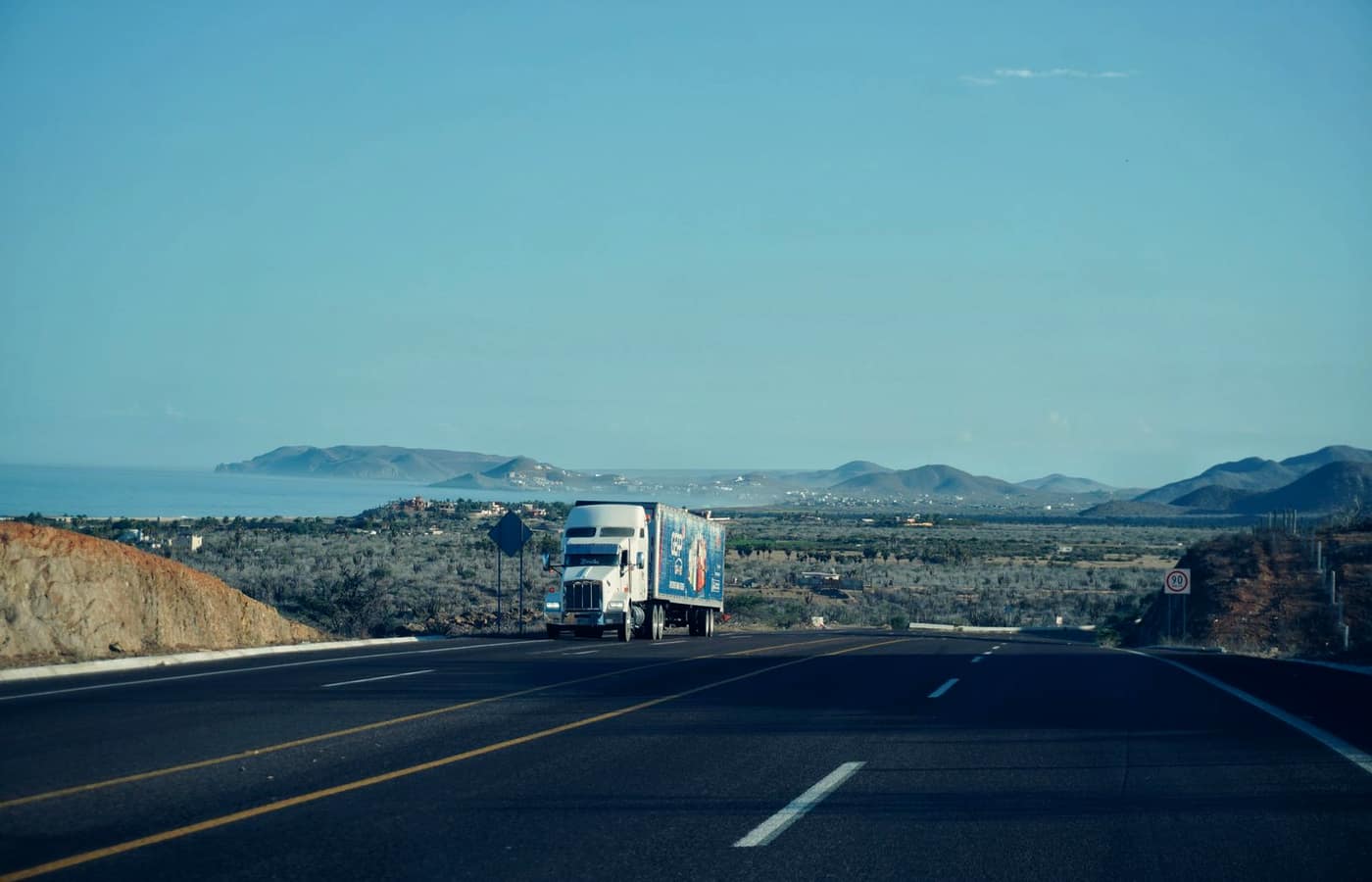 A semi truck on an open highway with mountains in the distance.