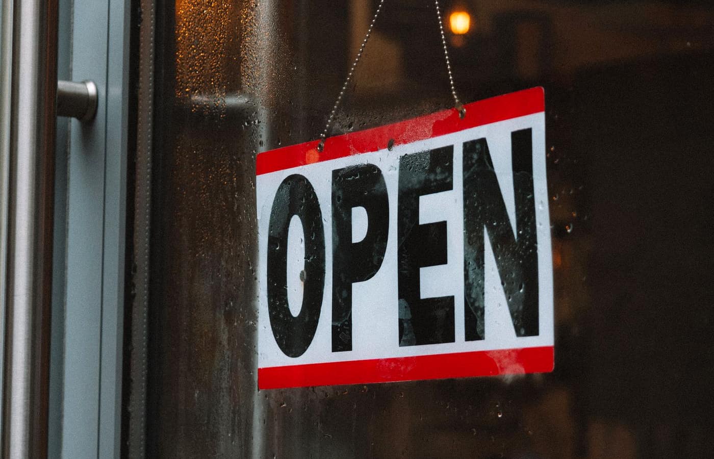 A red and white OPEN sign hanging on the glass door of a shop