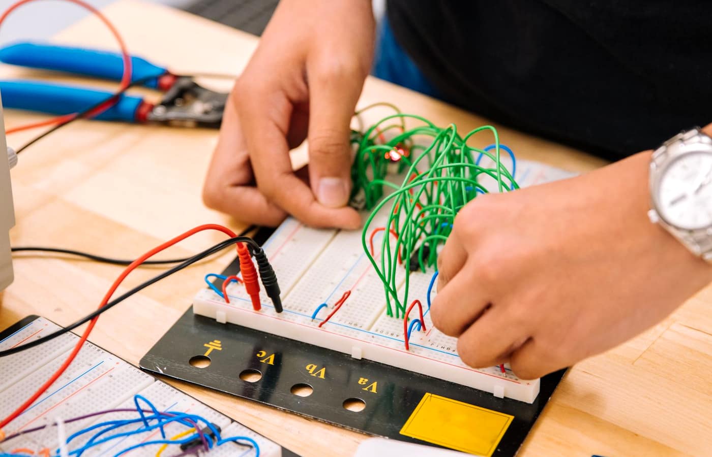 Hands wiring components onto an electronics breadboard with colored jumper wires.